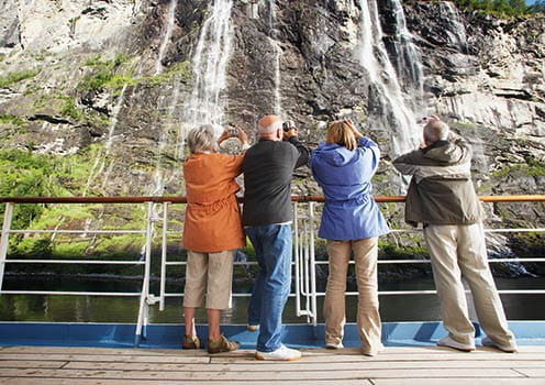 A group of tourists taking photos of a waterfall from the deck of a ship